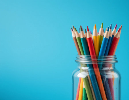 Colorful pencils in a glass jar on blue background with copy spaceの素材