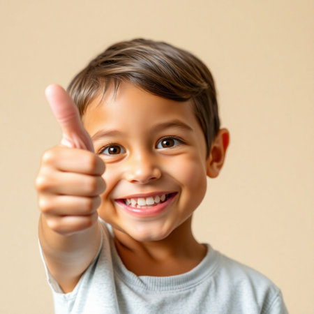 Closeup portrait of a cute little boy showing thumbs up gesture over beige backgroundの素材