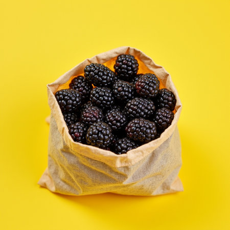 Blackberries in a paper bag on a yellow background, top viewの素材