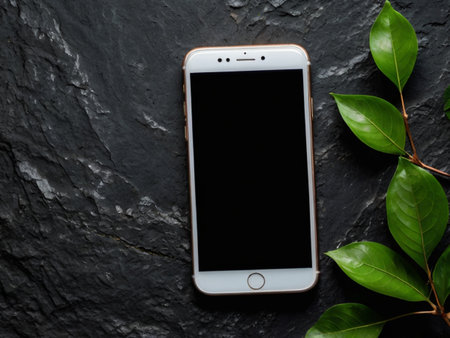 Smartphone with blank screen and green leaves on black stone background.の素材