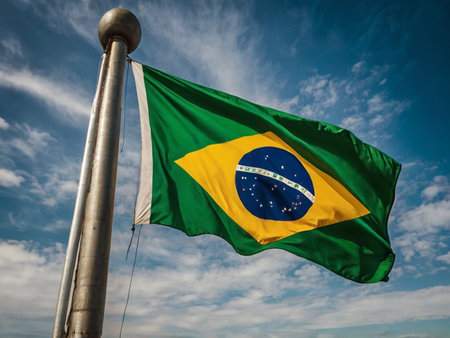 Brazilian flag waving in the wind against blue sky with white cloudsの素材