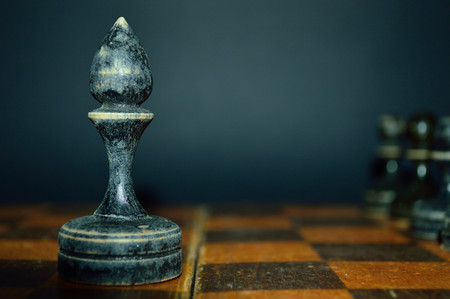 Old black wooden bishop on a chessboard. Perfect background for business.の写真素材
