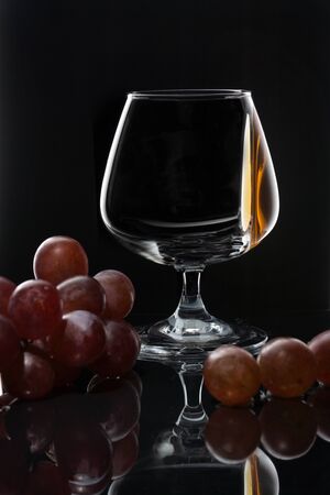 Cognac on the wall of a glass glass on a dark background with grapesの写真素材