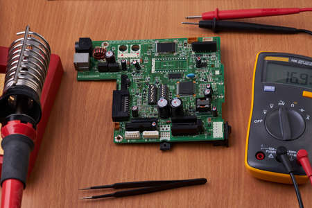 Electronic board repair component held with tweezers by an engineer over a green motherboard.の写真素材