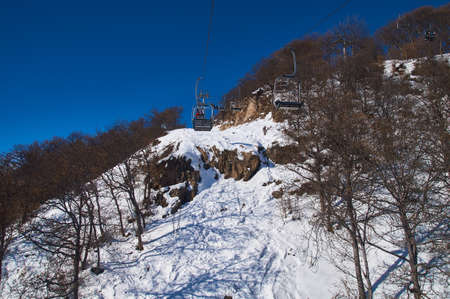 chairlift on the slope of the ski slope against the background of snowy mountains on a sunny dayの写真素材