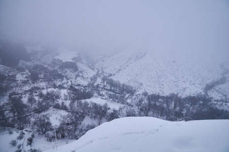 Snowy slopes of a mountain gorge covered with thick fogの写真素材