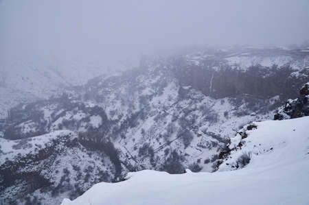Snowy slopes of a mountain gorge covered with thick fogの写真素材