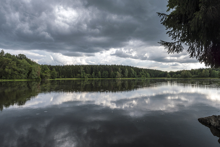 Lake in the middle of a forest with mirroring storm cloudsの写真素材