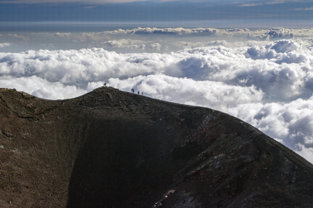 silhouettes of mountaineers over clouds at the edge of an extinct crater at the volcano Etna in Sicilyの写真素材