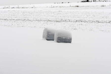 two forgotten bales of straw in deep snow on a meadow in winter in the highlandsの写真素材