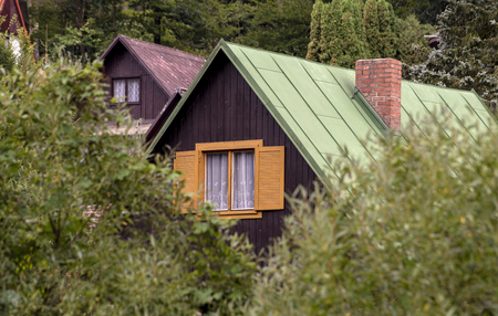 colorful roofs of two small houses with a chimney peeping between the trees in the woods background in the summerの写真素材