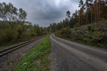 forest path next to train tracks under cloudy clouds in autumnの写真素材