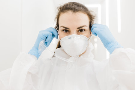 A beautiful doctor girl takes on her protective mask during an epidemic covid in the white corridor...