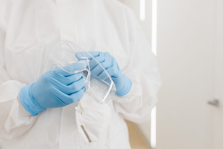 Protective medical goggles in the hands of a doctor in the white corridor of the hospital during...