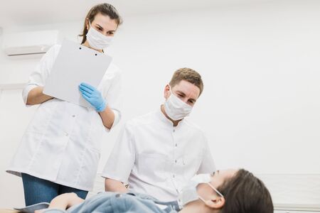 Two doctors examine a patient during an epidemic covid in the hospital. A girl doctor in a protective medical mask with a tablet.の写真素材