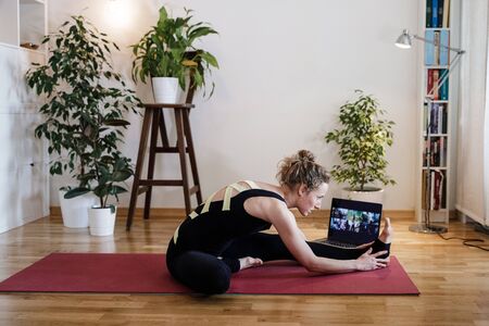 Girl does yoga in the apartment by video link in a beautiful designer apartment. Girl watches a tutorial on a laptop, athlete do yoga at home on self-isolationの写真素材