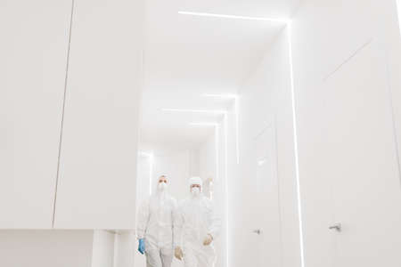 Two doctors in protective suits walk during an epidemic covid in the white corridor of the hospital.のeditorial素材