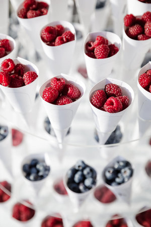 Ripe beautiful red raspberries and blueberry in white glasses. White packaging. Ripe raspberry...