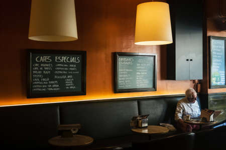 Barcelona, Spain. May 2020. A lonely elderly man sits alone in a cafe and reads a newspaper.のeditorial素材