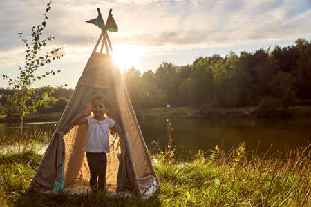 Girl at sunset in nature. Wigwam by lake. New home in hut. CHILDRENS GAMES.の写真素材