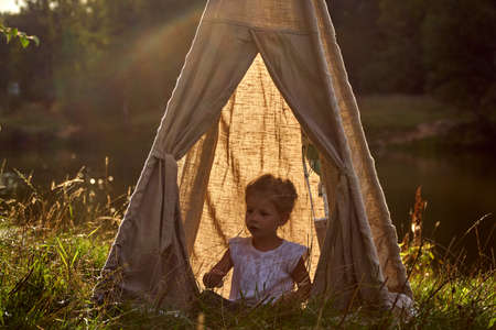 Girl at sunset in nature. Wigwam by lake. New home in hut. CHILDRENS GAMES.の写真素材