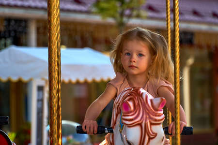 Serious child and brooding on a carousel horse. A cute girl is riding attractionの写真素材