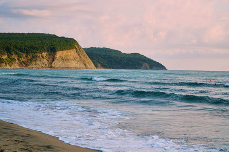 Blue water at the cliff and sandy shore. Calm and tranquility. Mountain by sea.