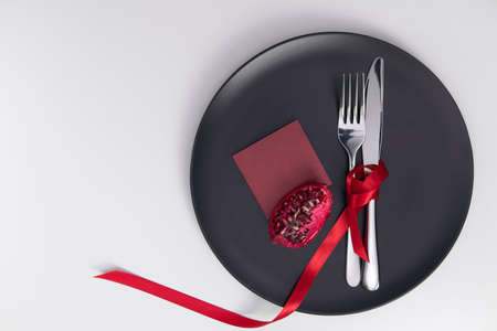 Festive table setting with fruits pomegranate. Ribbon on cutlery and stylish matte gray plate. Valentines Day. Holiday concept. Place for inscriptions. Greeting card with love Valentines Day.の写真素材