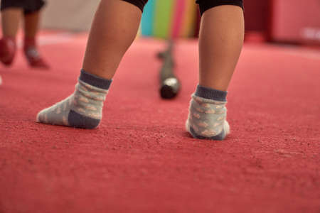 Childrens legs in the gym. Little feet of a child in blue socks for class. Childrens club with a carpet. Girl gymnast goes in for sports. Red mats in the gym.の写真素材