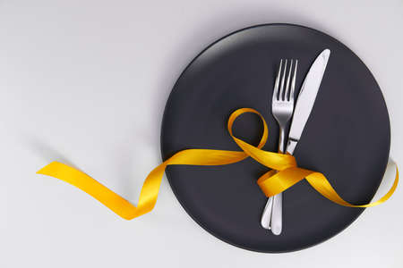 Table setting with gray plate and ribbon. Fork and knife for a holiday dinner on a holiday date. Place for taeksta on a white background.の写真素材