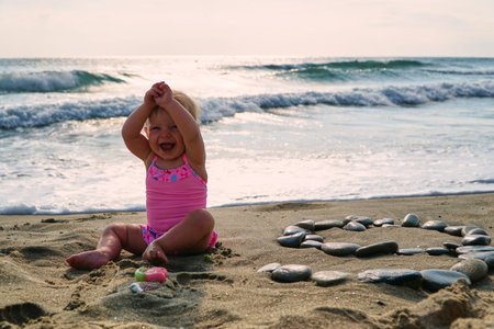 Happy baby in sand plays. Cheerful little kid playing on beach on sunny day.の写真素材