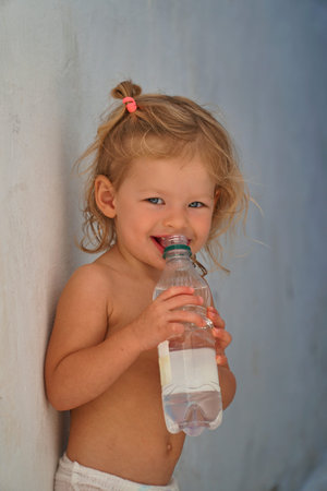 Baby girl in diapers drinks water from a bottle on the street. Funny kids games. Healthy food for babies. Happy Child drinks water.の写真素材