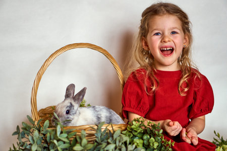 cheerful happy girl with easter bunny in a basket. Cute little girl holding cute fluffy rabbit...