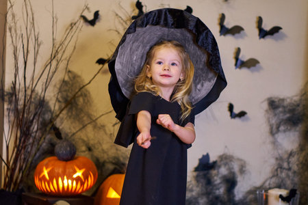 Halloween girl dressed as a witch with a hat and a magic wand. Black dress on a small child for a...