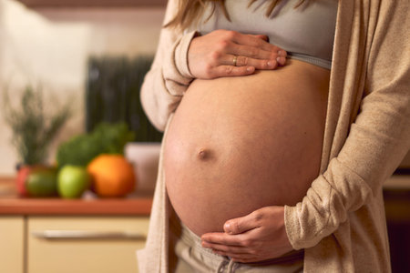 A pregnant woman in the kitchen holds her tummy. Expectant mother strokes and fresh vegetables and...