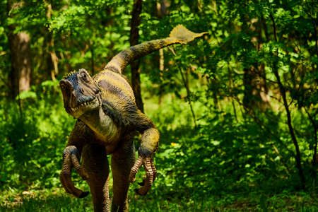 A dinosaur in Jurassic Park lives among the trees. Construction and model of dinosaurs in the forest. Live wild lizards hunt and survive. Battle and food scene in dino park.の写真素材