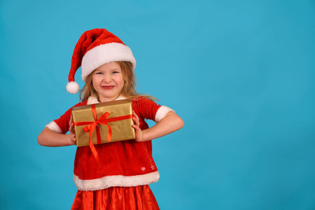 Funny Christmas child girl in santa claus cap is hold gift grimacing. Play with facial expressions....