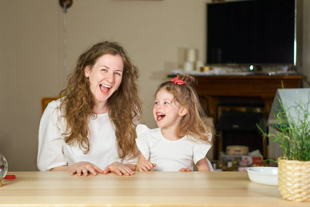 Have fun together. Smile and laugh at home. Happy family at the table. Motherhood is joy. Children laughter. Kids are playing. A woman babysitter is good for a sister. White dresses on caucasian womenの写真素材