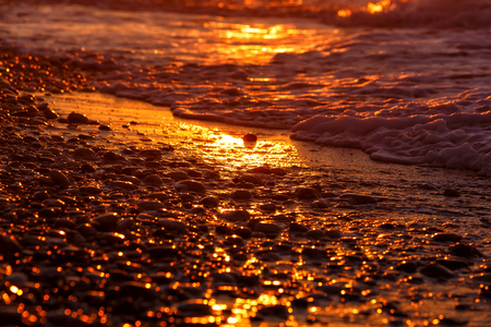 pebble beach close-up with surfing sea in a sunset lightの写真素材
