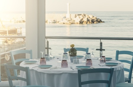 Tables and chairs at a waterfront bar with views across the harbour, Hersonissos, Crete, Greece, Europe.の写真素材