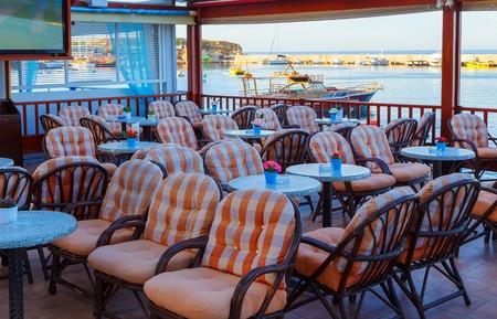 Tables and chairs at a waterfront bar with views across the harbour, Hersonissos, Crete, Greece, Europe.の写真素材
