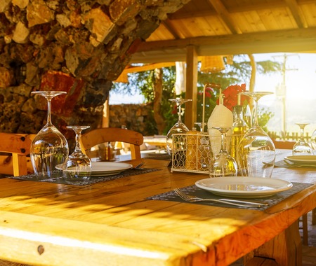 wooden table with glasses of Cutlery, flower in a glass decanter, on the background of a stone arch and sunlight. The concept of the Greek tavern. Crete, Greeceの写真素材