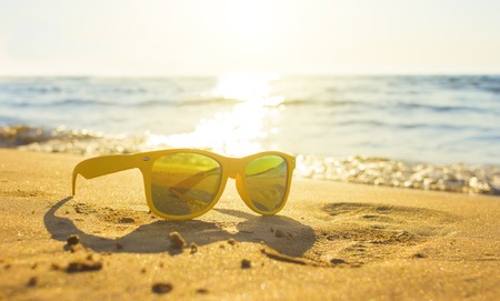 Yellow glasses the sea sand, sunglasses with beautiful sea scenery. sunglasses are reflected in the Golden wet sand as in the mirrorの写真素材