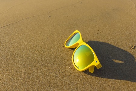 yellow stylish glasses on sandy beach, the concept of a resort holiday with a place for copyspaceの写真素材