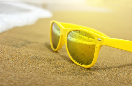 yellow stylish sunglasses on the beach in the sand and wavesの写真素材