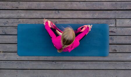 Top view of beautiful young fitness woman working out on wooden floor terrace, doing yoga exercise, full length.の写真素材