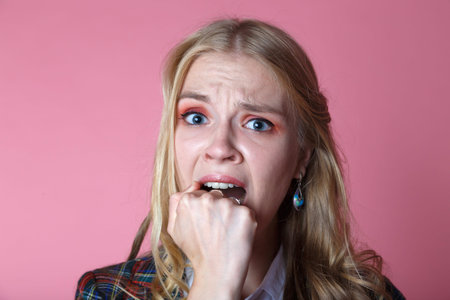 girl in fear closes fist open mouth, curly blonde on pink background.