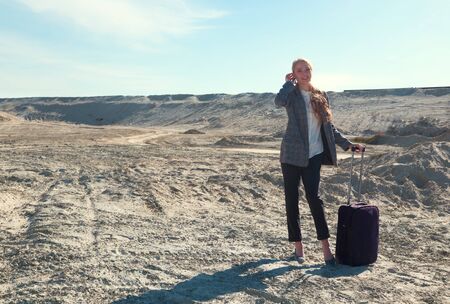 young blonde in office clothes with a suitcase in the desert among the Sands. The concept of home away from homeの写真素材