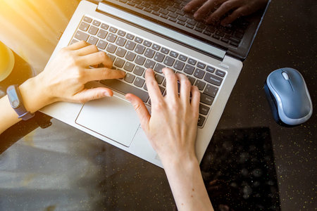 top view of woman's hands typing on laptop with notebook and items on black background