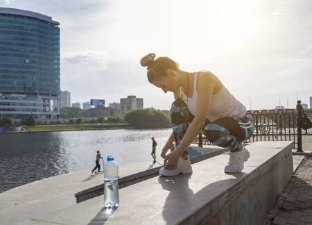Young modern woman tying running shoes in urban landscape of modern megapolisの写真素材